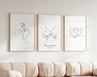 May include: Three black and white line art prints in wooden frames. The prints depict a couple's faces, two hands holding each other's pinky fingers, and two intertwined hearts. The middle print includes the text "Marcus & Laura It's Always Been You 20.03.2023".