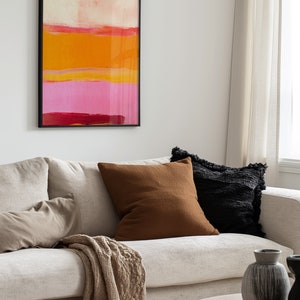 Puede incluir: Un sof&aacute; blanco con cojines marrones y negros, una manta de tiro beige y una mesa de caf&eacute; de madera. Un cuadro abstracto enmarcado con rayas rosas, naranjas y rojas cuelga en la pared detr&aacute;s del sof&aacute;.