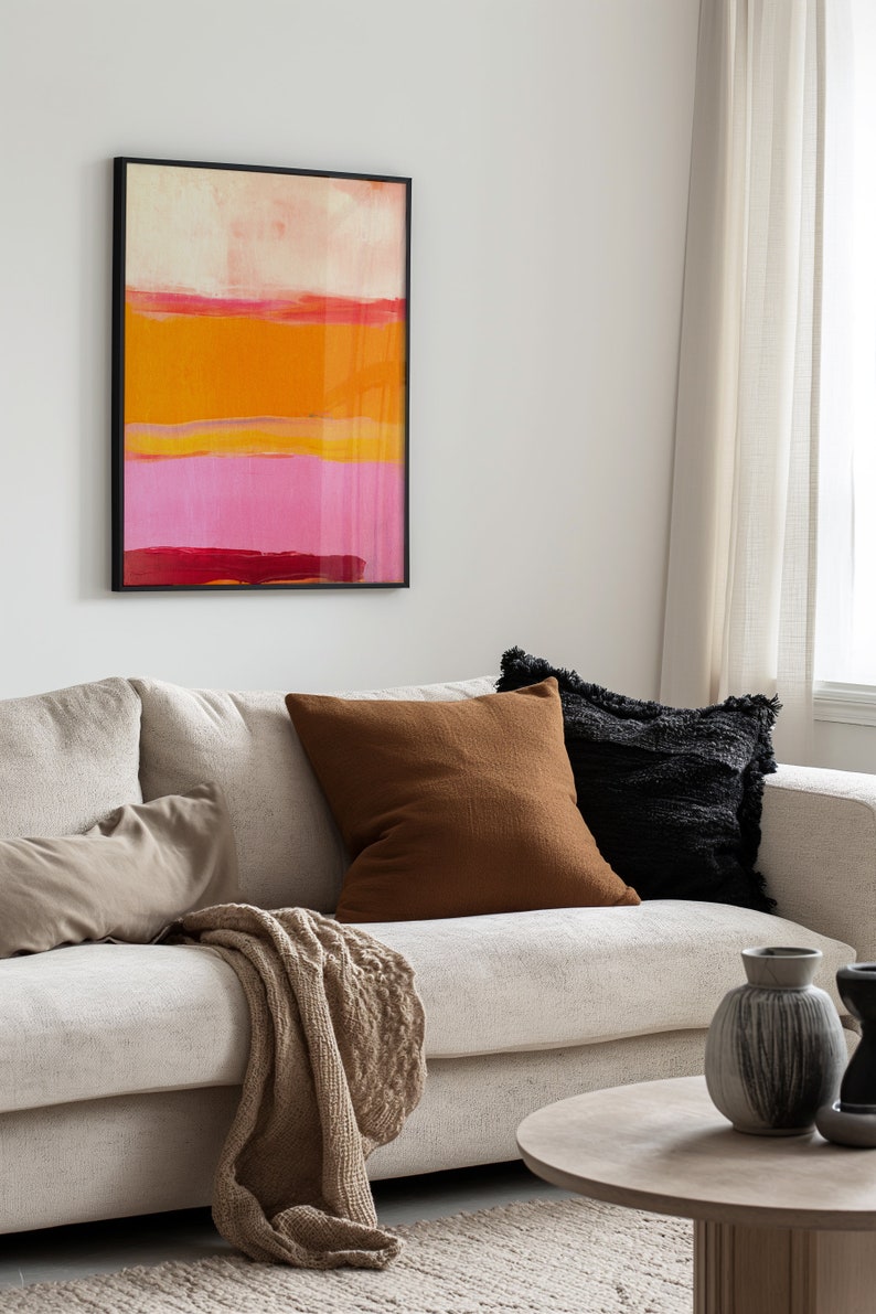 Puede incluir: Un sof&aacute; blanco con cojines marrones y negros, una manta de tiro beige y una mesa de caf&eacute; de madera. Un cuadro abstracto enmarcado con rayas rosas, naranjas y rojas cuelga en la pared detr&aacute;s del sof&aacute;.