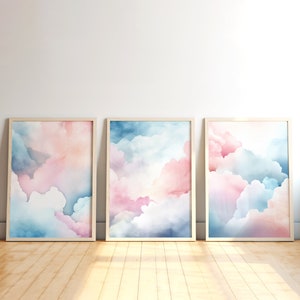 Puede incluir: Tres pinturas de acuarela enmarcadas de nubes rosas y azules. Las pinturas están en marcos de madera y están colgadas en una pared blanca.