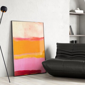 Puede incluir: Una l&aacute;mpara de pie de tr&iacute;pode negra con tres luminarias redondas de color dorado. La l&aacute;mpara est&aacute; en una sala de estar con un sof&aacute; de cuero negro y una pintura abstracta con tonos naranja, rosa y rojo.