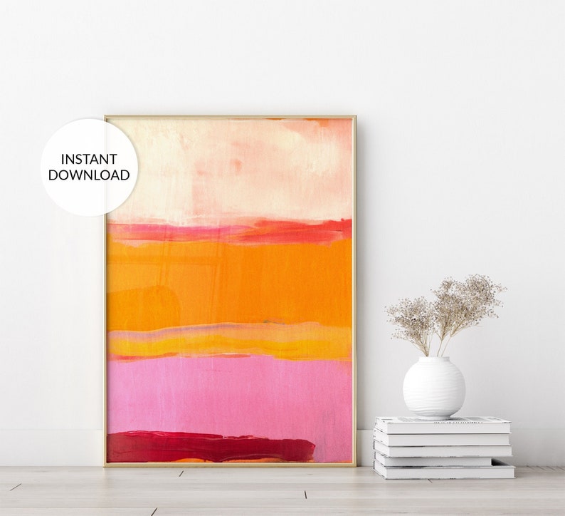 Colorful modern poster in orange, pink, and red, framed and standing on the floor.