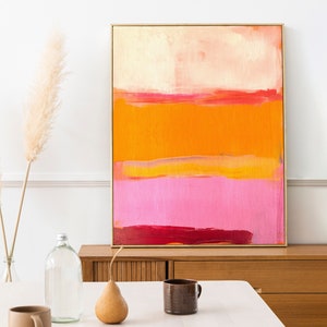 Puede incluir: Pintura abstracta con rayas horizontales en tonos de rosa, naranja y amarillo. La pintura est&aacute; enmarcada en oro y est&aacute; colgada en una pared blanca.