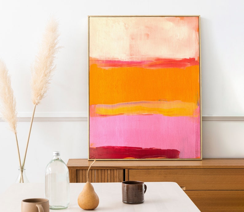Puede incluir: Pintura abstracta con rayas horizontales en tonos de rosa, naranja y amarillo. La pintura est&aacute; enmarcada en oro y est&aacute; colgada en una pared blanca.