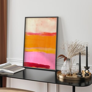 Puede incluir: Impresi&oacute;n de arte abstracto en un marco negro con un esquema de color rosa, naranja y amarillo. La impresi&oacute;n est&aacute; colgada en una pared blanca sobre una mesa negra con art&iacute;culos decorativos.
