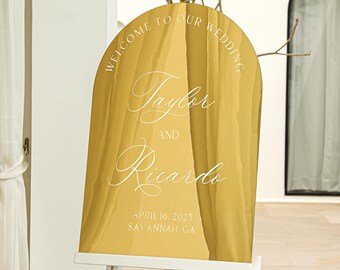 May include: Gold arch-shaped welcome sign with the text "Welcome to our wedding" at the top, followed by the names "Taylor and Ricardo" in cursive script. The date "April 16, 2023" and location "Savannah, GA" are printed below the names.