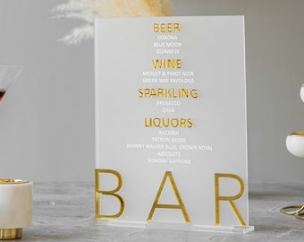May include: A clear acrylic sign with gold lettering that reads "BEER", "WINE", "SPARKLING", "LIQUORS", and "BAR". The sign lists various beer, wine, sparkling wine, and liquor brands.
