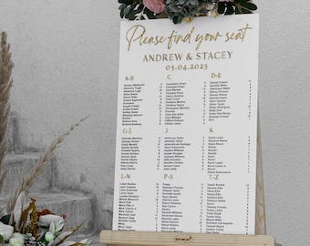 Könnte beinhalten: Ein weißer Sitzplan mit goldenen Buchstaben auf einem Staffelei. Der Plan listet die Namen der Gäste in alphabetischer Reihenfolge mit Tischzuweisungen auf. Der Plan ist mit Blumen und Grünpflanzen dekoriert. Der Text auf dem Plan lautet "Bitte finden Sie Ihren Platz", "Andrew & Stacey" und "03.04.2023".