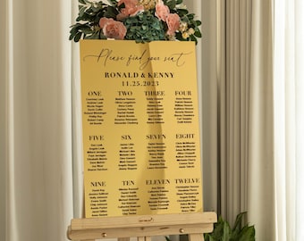 Könnte beinhalten: Goldene Sitzordnung mit dem Text "Please find your seat" und "Ronald & Kenny 11.25.2023". Die Karte listet die Namen der Gäste nach Tischnummer von eins bis zwölf auf.