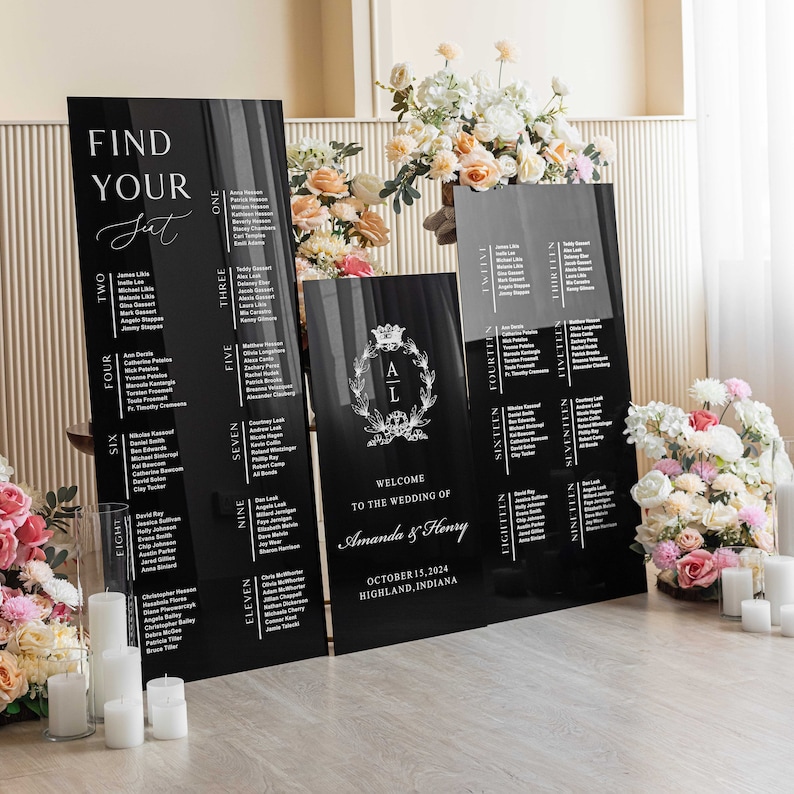 May include: Black acrylic wedding seating chart signs with white text. The signs are arranged in a row on a wooden floor. The signs include the names of guests and table numbers. The signs also include the text "Find Your Seat", "Welcome to the Wedding of Amanda & Henry", "October 15, 2024", and "Highland, Indiana".