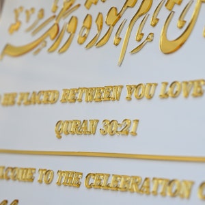 Puede incluir: Un cartel blanco con letras doradas que dice "To be placed between you love Quran 30:21" y "Welcome to the celebration of" con una escritura cursiva dorada en la parte inferior.