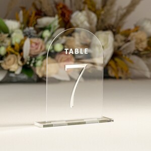 May include: Clear acrylic table number holder with a rounded top and a base. The number 7 is printed in silver on the front. The text "TABLE" is printed in white at the top.