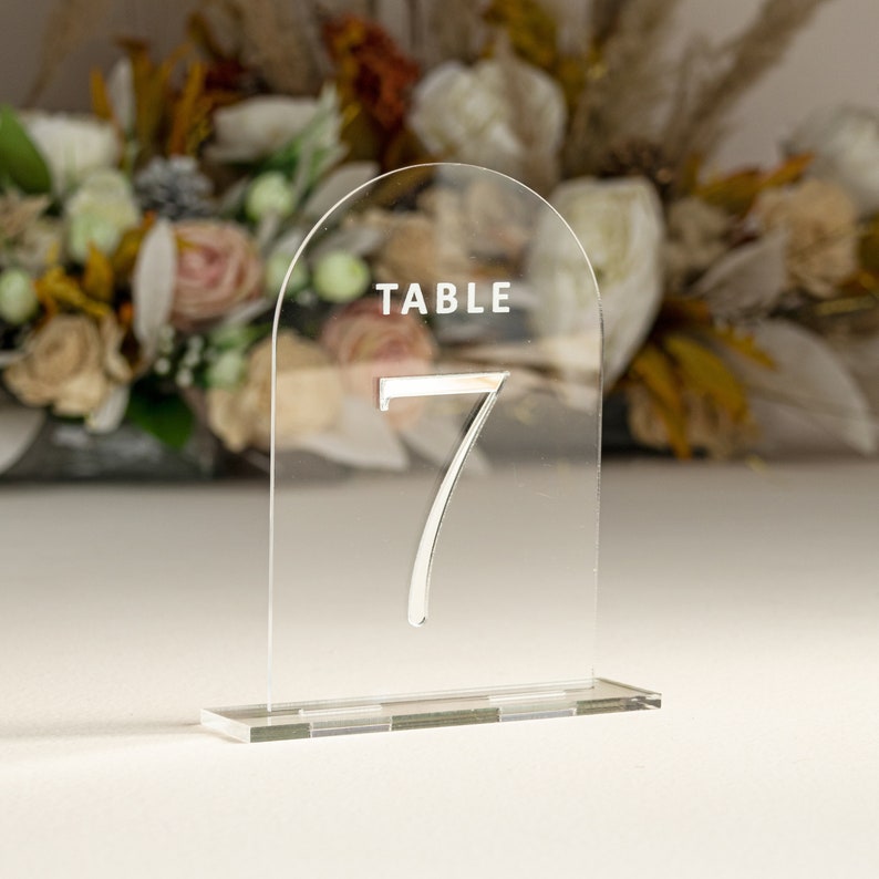 May include: Clear acrylic table number holder with a rounded top and a base. The number 7 is printed in silver on the front. The text "TABLE" is printed in white at the top.