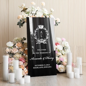 May include: Black welcome sign with white text and a floral monogram. The text reads "Welcome to the wedding of Amanda & Henry, October 15, 2024, Highland, Indiana".