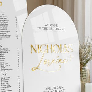 Puede incluir: Un letrero de bienvenida de boda blanco en forma de arco con letras doradas en 3D que dicen "WELCOME TO THE WEDDING OF NICHOLAS Loraine +", con la fecha "APRIL 10, 2025" y la ubicaci&oacute;n "WILLINGTON, CT" impresas en negro abajo.