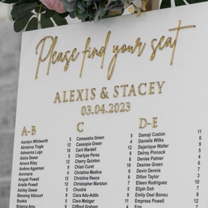 May include: A white seating chart with gold lettering for a wedding reception. The chart is titled "Please find your seat" and lists the names of guests under the headings "A-B", "C", and "D-E". The wedding date is listed as "03.04.2023" and the couple's names are listed as "Alexis & Stacey".