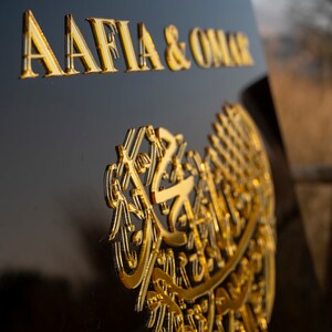 May include: A black sign with gold lettering that reads "To Our Wedding Aafia & Omar". The sign also features a gold heart-shaped design with intricate Arabic calligraphy.