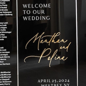 May include: Black wedding sign with gold lettering. The sign says "Welcome to our wedding" and "Marthan and Pefina" with the date "April 25, 2024" and location "Westbey, NY".
