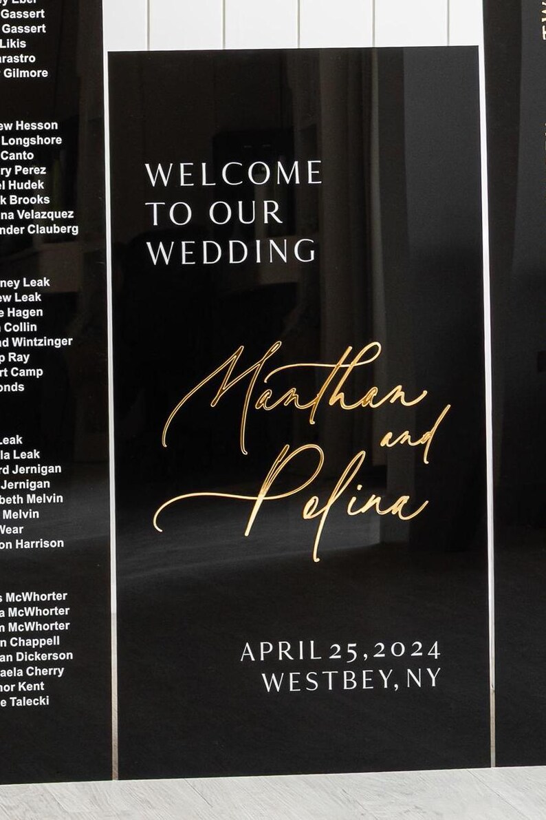 May include: Black wedding sign with gold lettering. The sign says "Welcome to our wedding" and "Marthan and Pefina" with the date "April 25, 2024" and location "Westbey, NY".