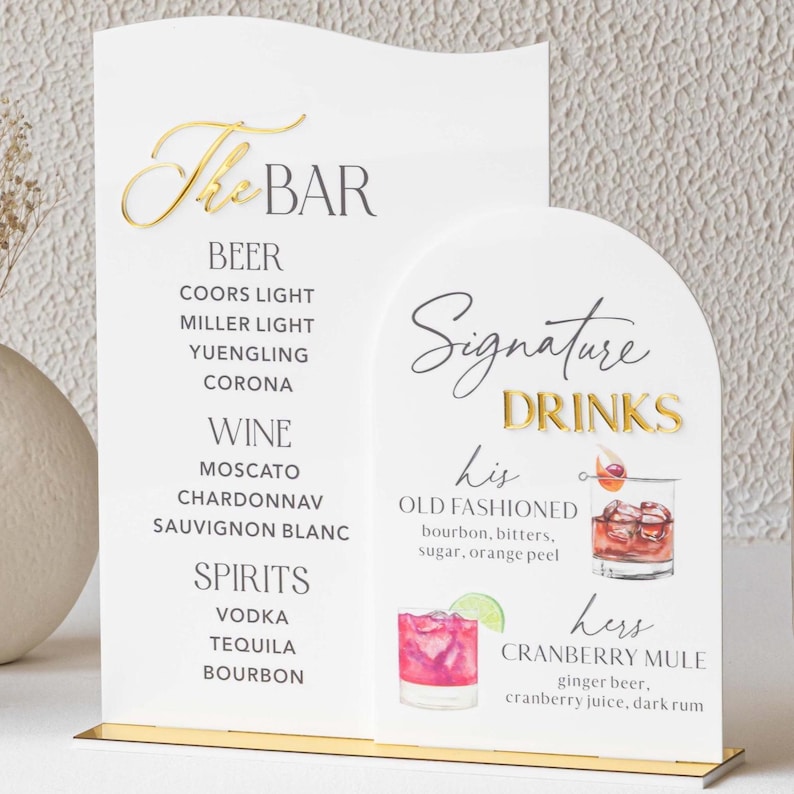 May include: A white bar menu sign with gold lettering and a gold base. The sign lists beer, wine, and spirits, along with signature drink recipes for an Old Fashioned and a Cranberry Mule.