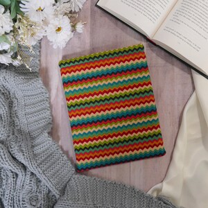Puede incluir: Una cubierta de libro colorida con un patrón de chevron en tonos de rojo, naranja, amarillo, verde, azul y marrón. La cubierta está hecha de tela y tiene una superficie ligeramente texturizada.