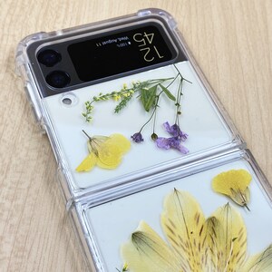 May include: A clear plastic phone case with a floral design. The case has a built-in mirror and a date display that reads "12.04 Wed. August 11 100%".