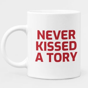 May include: White ceramic mug with a curved handle. The mug features the red text "NEVER KISSED A TORY" in a bold, sans-serif font. The mug is designed for hot beverages.