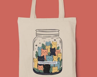 May include: A white tote bag with a design of a glass jar filled with cartoon cats. The jar has a label that reads "ANTIDEPRESSANTS".