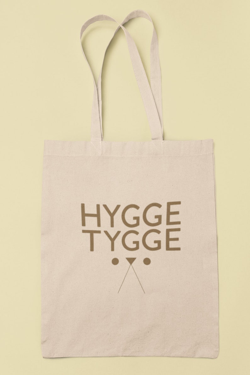 May include: A beige canvas tote bag with brown straps and the text "HYGGE TYGGE" printed on the front. The text is in a bold, sans-serif font.