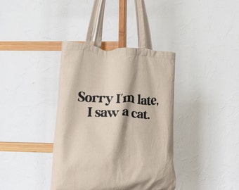 May include: A beige tote bag with black text that reads "Sorry I'm late, I saw a cat."