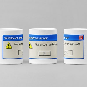 May include: White ceramic mug featuring a blue and white Windows error message that reads "Not enough caffeine!" with a yellow exclamation point icon. The message is in a blue box with a white "OK" button.