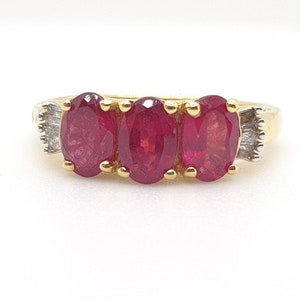 May include: A gold ring with three oval-shaped red rubies and small diamonds on the sides.