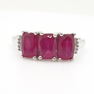 May include: A silver ring with three rectangular ruby gemstones set in a row. The ring has a white metal band.