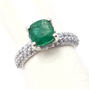 Puede incluir: Un anillo de plata con una gran piedra preciosa verde esmeralda rodeada de piedras blancas más pequeñas.
