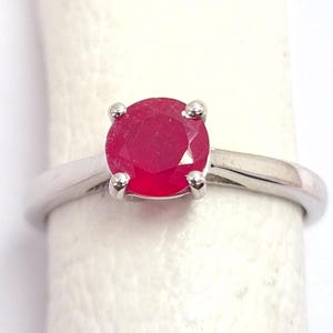 以下が含まれることがあります： 丸い鮮やかな赤い宝石をあしらったシルバーリング。 宝石は4つの小さな爪で固定されています。 リングバンドはシンプルな磨かれたシルバーです。