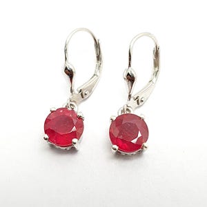 May include: A pair of silver dangle earrings with red ruby gemstones. The earrings have a lever back closure.