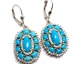 May include: A pair of silver-toned drop earrings featuring a central oval turquoise cabochon surrounded by a halo of smaller round turquoise stones and a border of clear sparkling crystals, finished with secure lever-back closures for pierced ears.