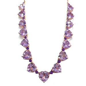 May include: A gold-toned necklace featuring heart-shaped purple gemstones. The necklace has a delicate chain and is adorned with multiple heart-shaped stones and smaller purple accents, creating a romantic and elegant design.