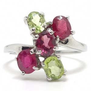 Puede incluir: Un anillo de plata con cinco piedras preciosas. El anillo tiene dos piedras rojas, dos piedras verdes y una piedra rosa.