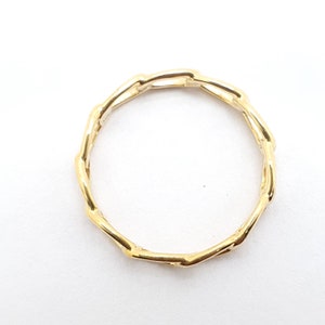 K&ouml;nnte beinhalten: Ein goldener Ring mit einem einzigartigen, ineinandergreifenden Kettendesign. Der Ring ist aus glattem, poliertem Metall gefertigt und hat einen schlichten, eleganten Stil.