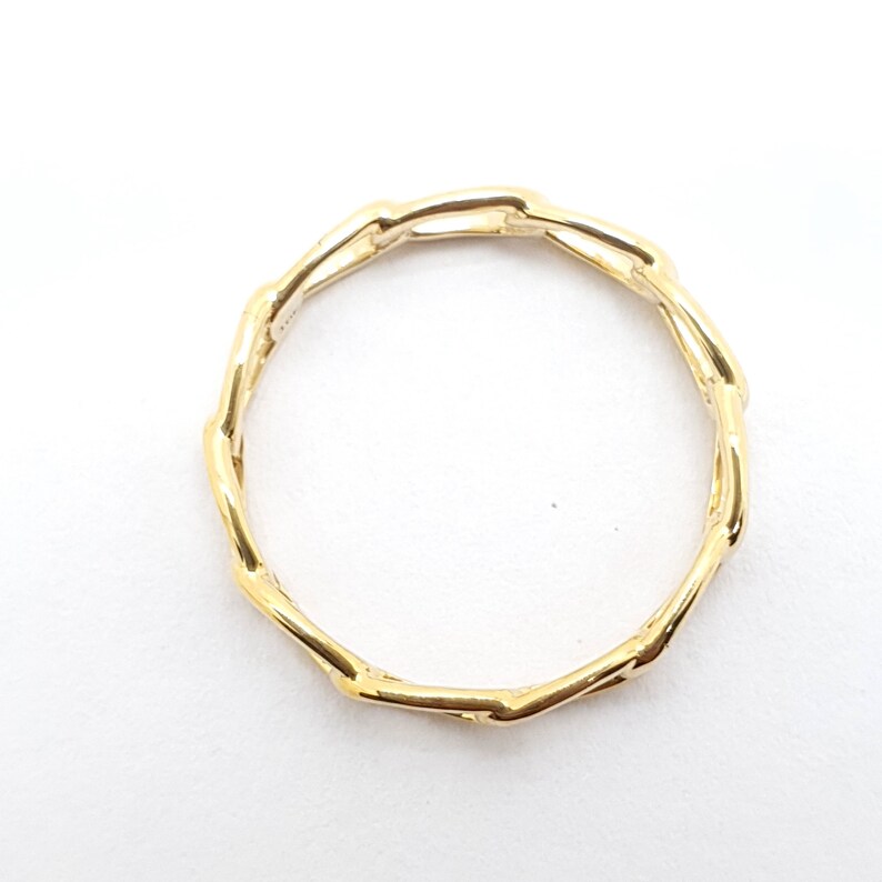 K&ouml;nnte beinhalten: Ein goldener Ring mit einem einzigartigen, ineinandergreifenden Kettendesign. Der Ring ist aus glattem, poliertem Metall gefertigt und hat einen schlichten, eleganten Stil.