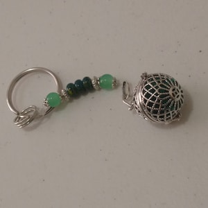 Könnte beinhalten: Ein silberner Schlüsselanhänger mit einem grünen und blauen Perlenanhänger und einem silbernen, durchbrochenen, kugelförmigen Anhänger.