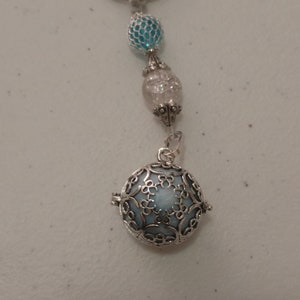 Könnte beinhalten: Ein silberner Schlüsselanhänger mit einem blauen und weißen, gemusterten Anhänger. Der Anhänger ist eine Kugel mit einem filigranen Metalldesign. Der Schlüsselanhänger hat auch zwei kleinere Perlen, eine blaue und eine weiße.