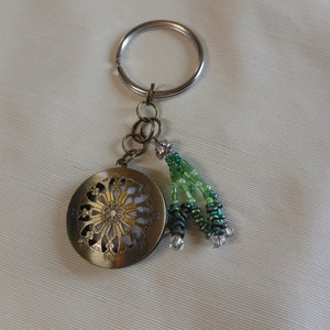 Puede incluir: Un llavero de latón con un dije circular que presenta un diseño decorativo y un borla de cuentas verdes.