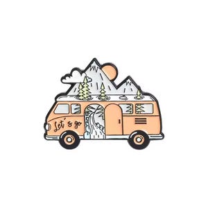 May include: An enamel pin featuring an orange camper van with the text "Let's go." The van has a mountain range, trees, and a sun on top. The pin is outlined in black and has black wheels.