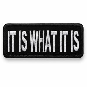 Pode incluir: Um emblema retangular bordado com fundo preto e borda branca. O texto IT IS WHAT IT IS está bordado em letras maiúsculas brancas no centro do emblema. O emblema possui cantos arredondados e uma borda limpa e bem acabada.