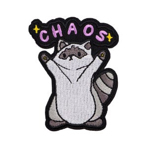 Pode incluir: Patch bordado com um guaxinim de desenho animado com os braços levantados. O guaxinim é branco e cinza, com um contorno preto. Acima do guaxinim está a palavra "CHAOS" em rosa, com estrelas amarelas. O patch tem uma borda preta.