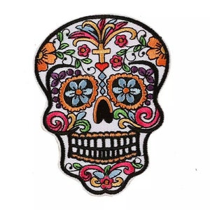 Op de afbeelding: Gestikt suiker schedel patch met kleurrijke bloemdetails, een kruis en een hart. De schedel is wit met zwarte ogen en een zwarte mond.