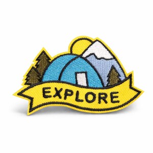 Könnte beinhalten: Gestickter Aufnäher mit gelbem Banner und der Aufschrift "EXPLORE". Der Aufnäher zeigt ein blaues Zelt, einen Berg mit schneebedeckter Spitze, eine gelbe Sonne und grüne Bäume. Camping-Thema.