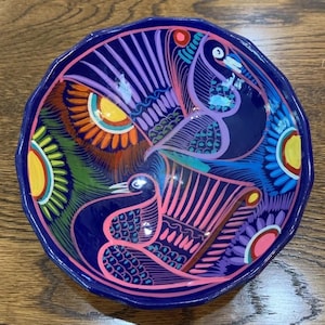 May include: A blue ceramic bowl with a colourful hand-painted design of birds and flowers. The bowl is decorated with bright colours, including yellow, orange, red, green, blue, purple, and pink.